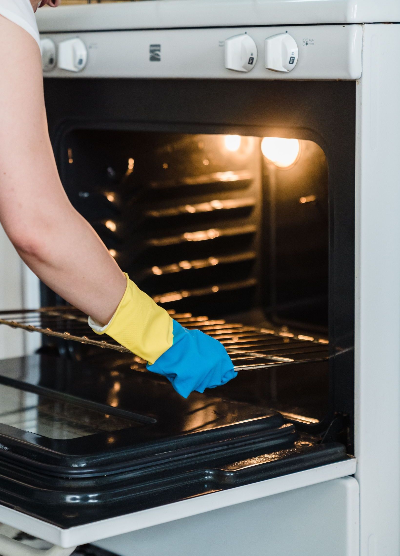 Adult woman cleaning an oven using protective rubber gloves indoors.